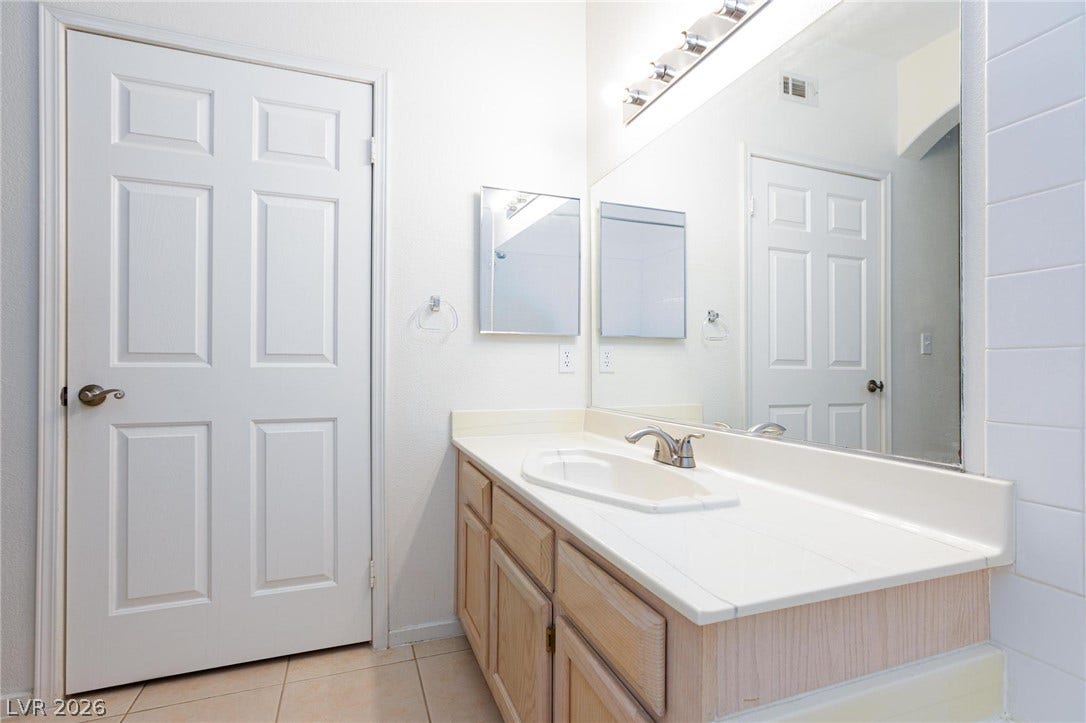 A spacious vanity with a large mirror and neutral tile flooring defines this bathroom.