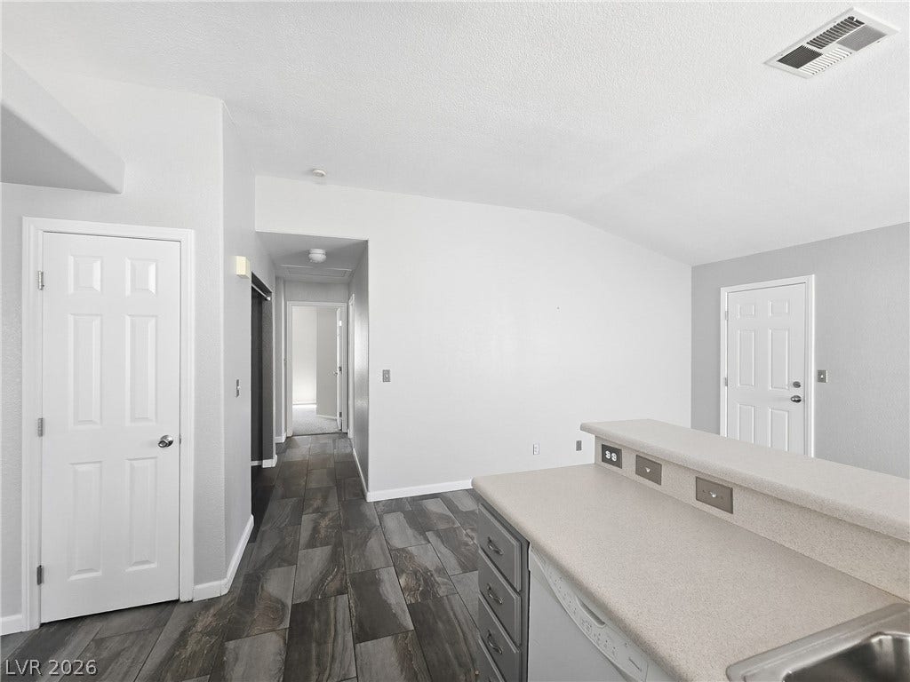 A breakfast bar opens to neutral interiors with dark tile-style flooring and high ceilings.