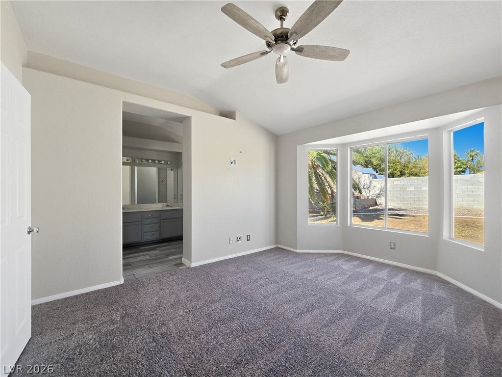 An angled bay window overlooks the backyard, flooding this carpeted bedroom with natural light.