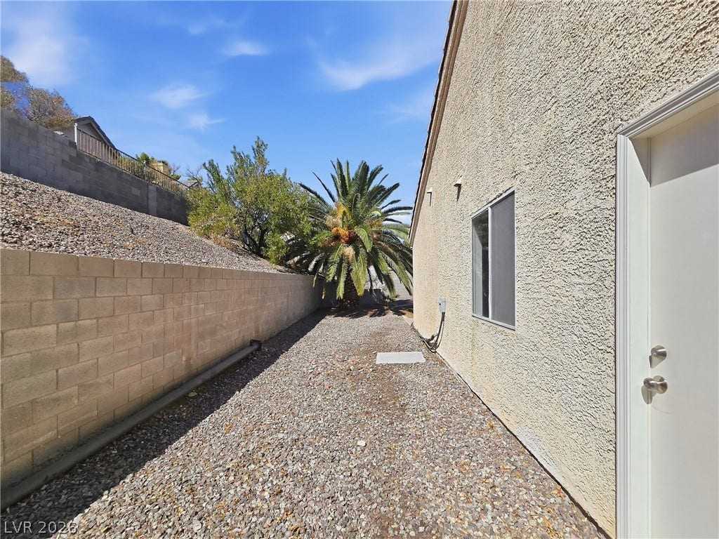 A low-maintenance gravel path runs alongside the stucco exterior, bordered by a block wall.