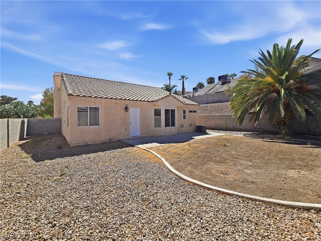 An open backyard space bordered by stucco walls features gravel landscaping and a tiled roofline.