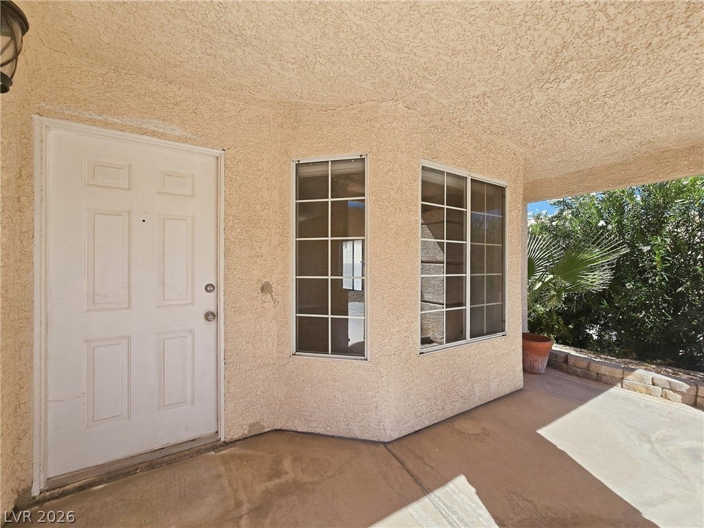 Textured stucco walls and concrete flooring frame this welcoming covered entry porch.