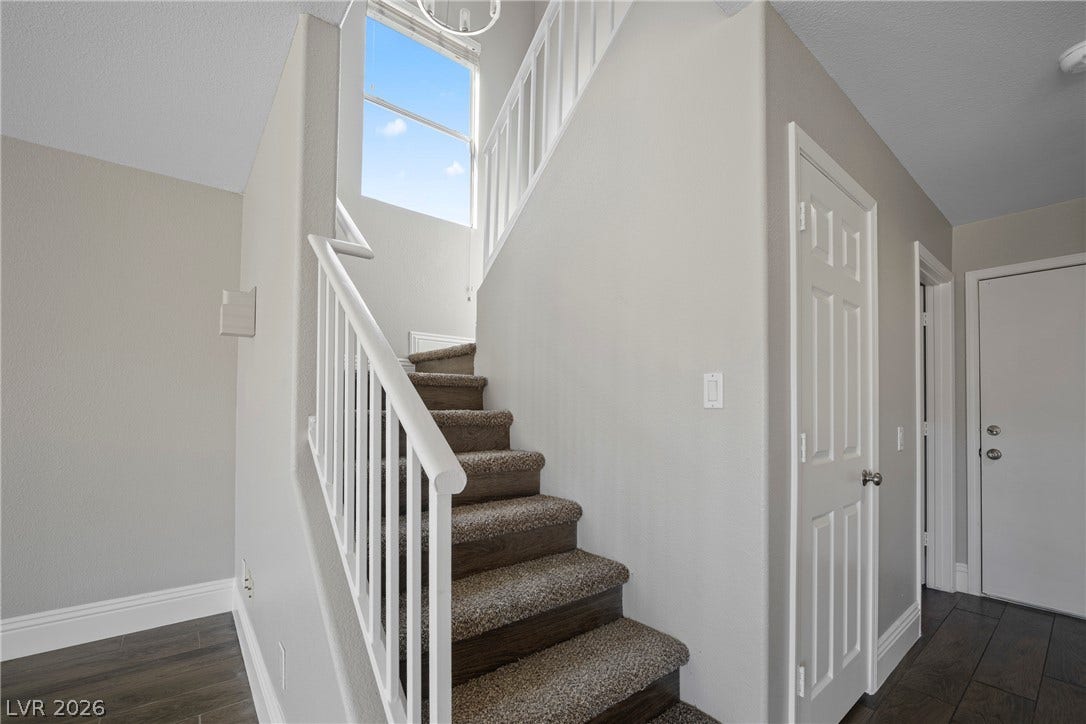 Natural light streams through a high window onto the carpeted staircase and neutral entryway flooring.