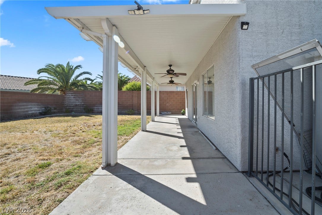 An expansive covered concrete patio overlooks the private backyard under clear blue skies.