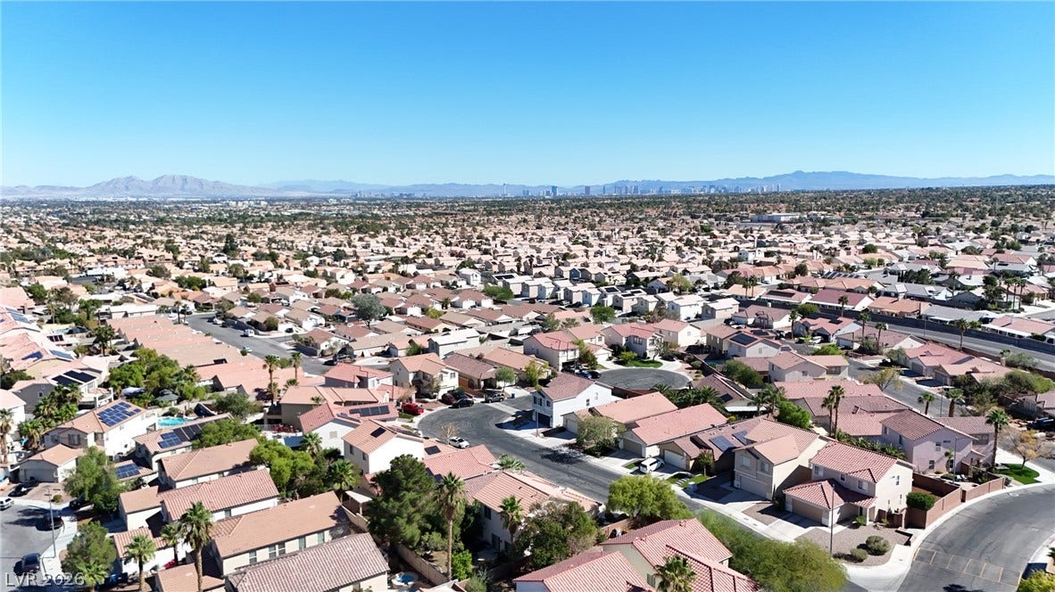A sweeping bird's-eye view captures the suburban neighborhood structure under a clear blue sky.