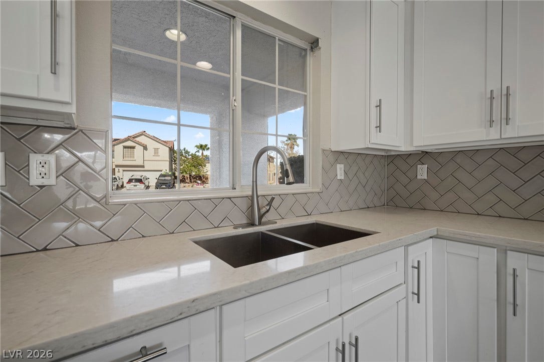 A stylish tiled backsplash and solid stone countertops surround the double basin kitchen sink.