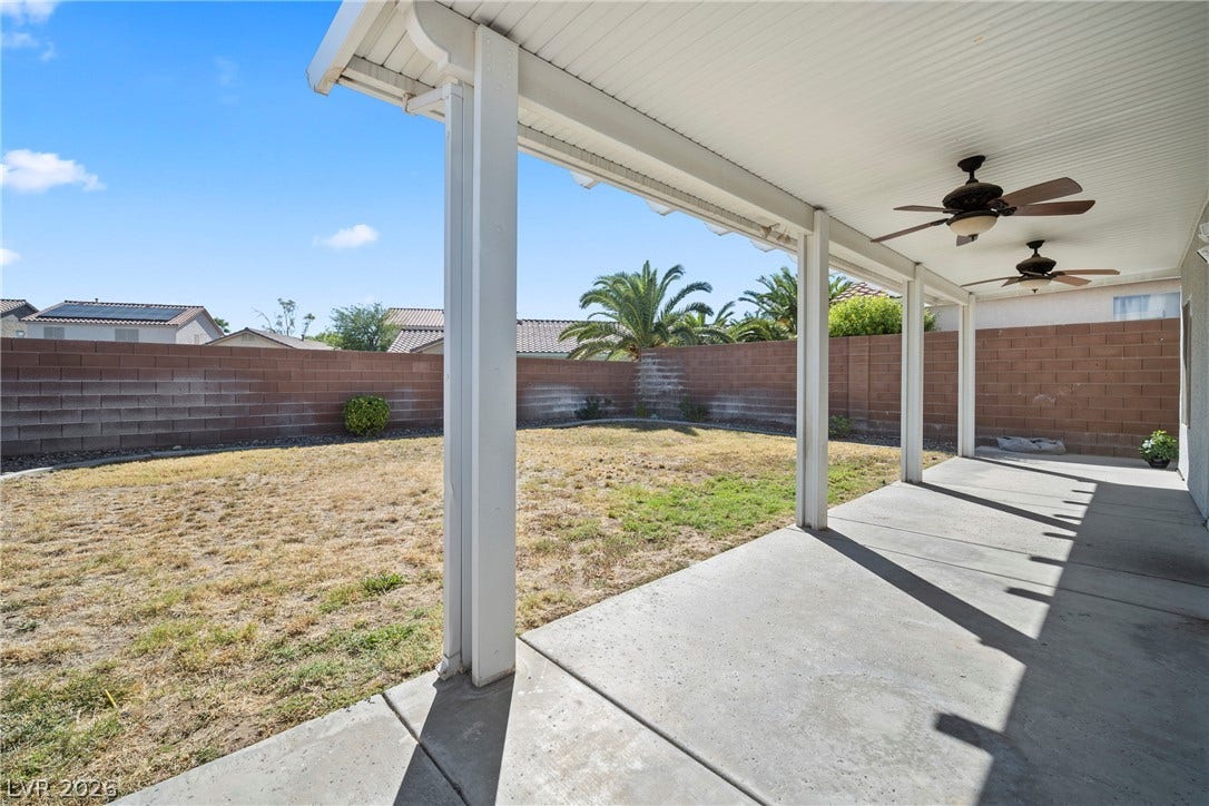 A spacious covered concrete patio overlooks the private backyard enclosed by brick fencing.