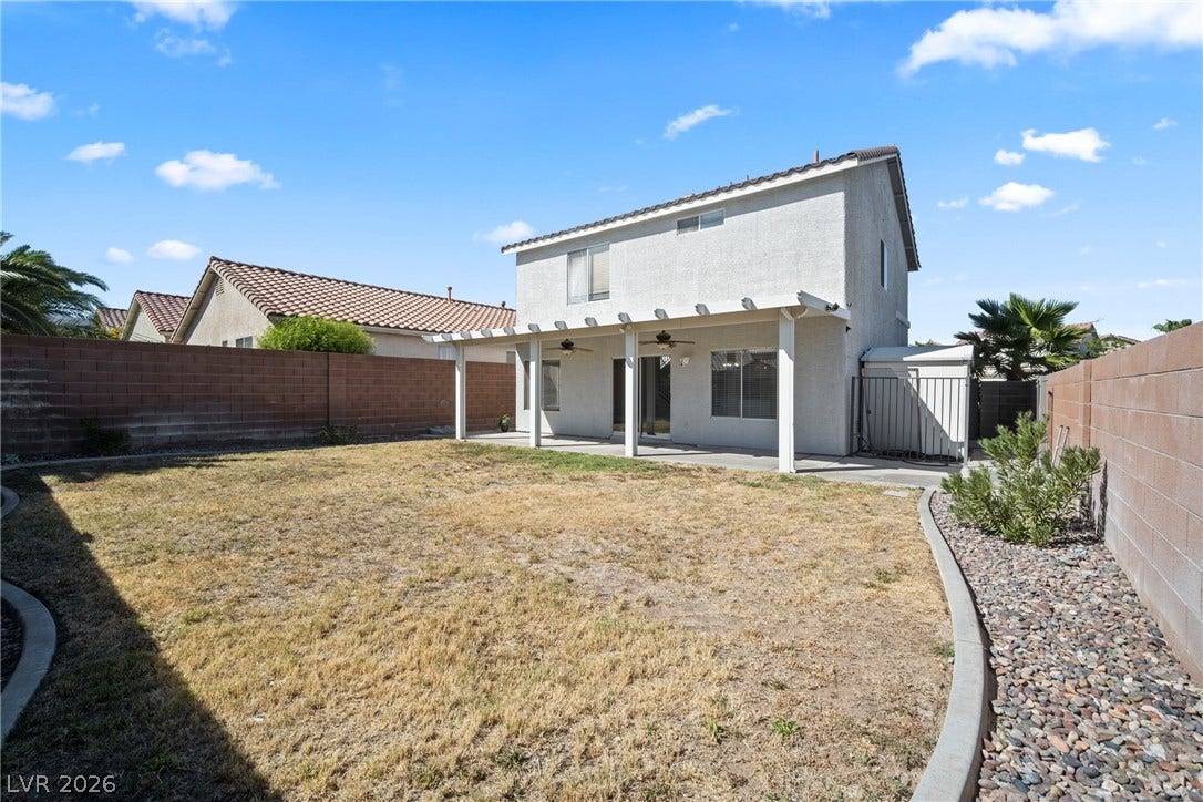 A spacious backyard features a covered patio and block wall fencing under blue skies.