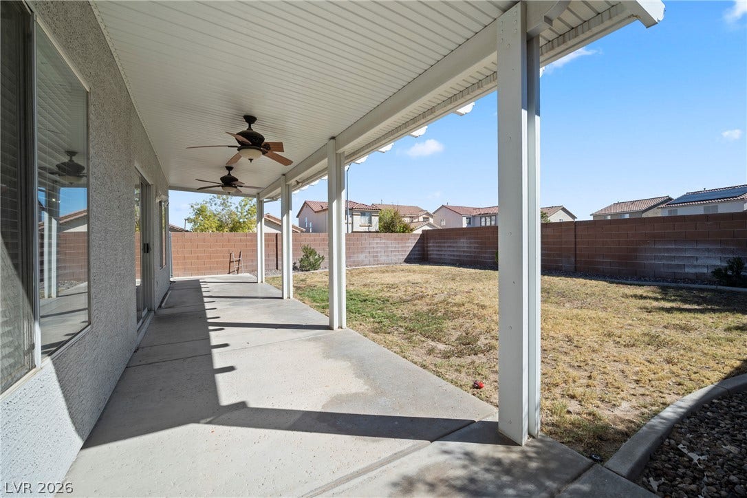 A covered concrete patio overlooks the walled backyard under clear skies.