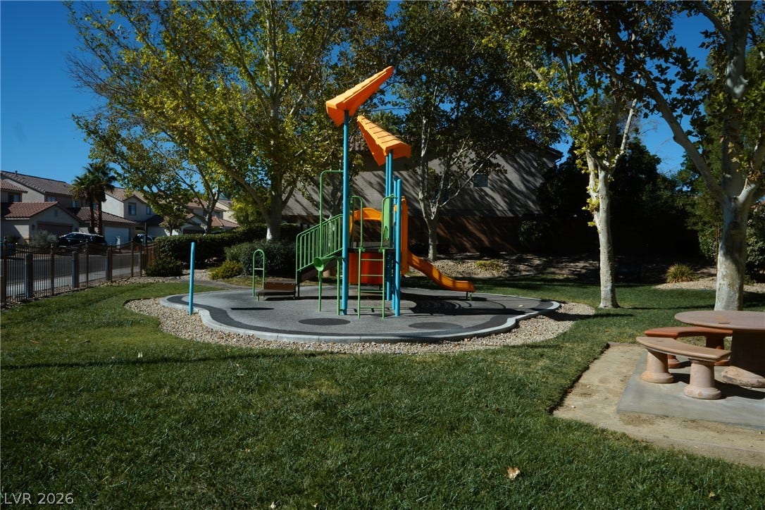 Lush grassy grounds surround a neighborhood play area shaded by mature trees.