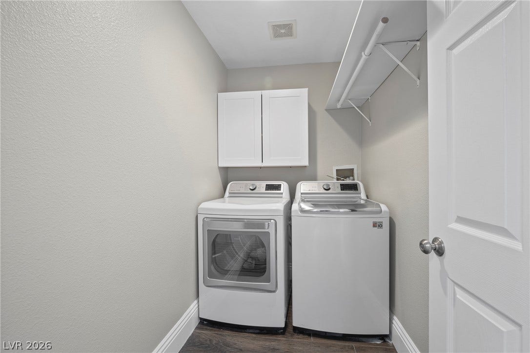 Functional laundry space features overhead cabinetry, shelving, and wood-look flooring.