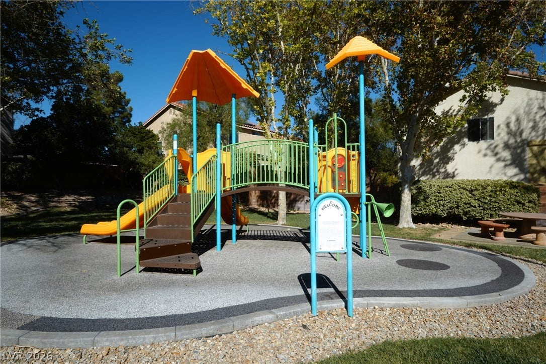 A well-maintained neighborhood playground sits nestled among mature trees under a clear blue sky.