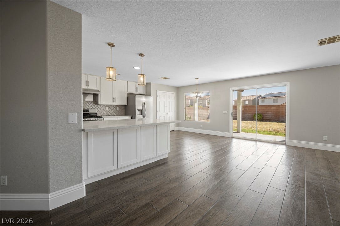 Gleaming wood-look tile floors stretch across a wide, open-concept living space toward sliding glass doors.