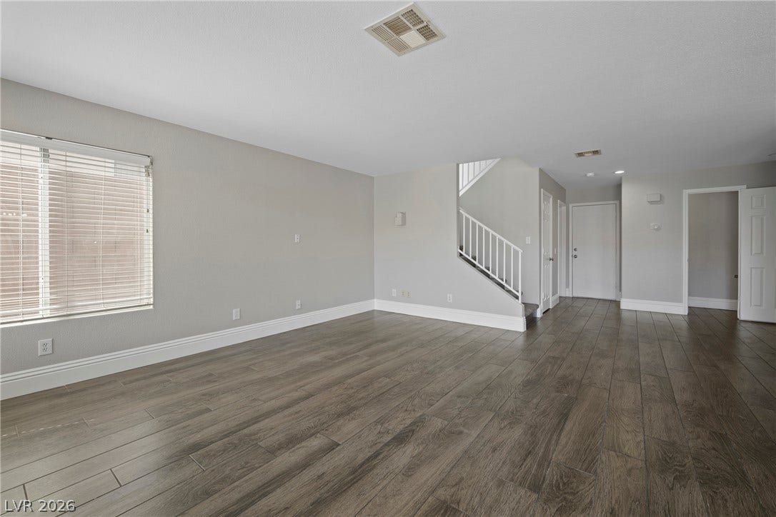 Plank flooring anchors the open living space, leading past a staircase toward the entryway.