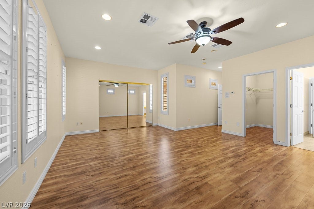 This spacious room features rich wood flooring, crisp window shutters, and ample closet space with mirrored doors.