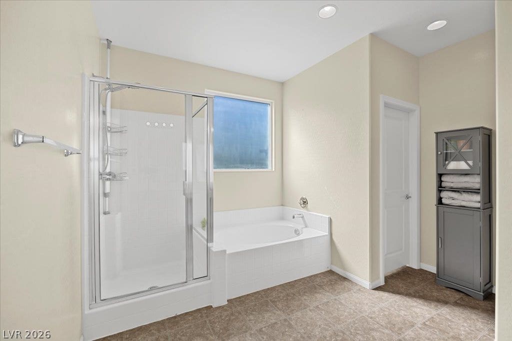 Tile flooring and recessed lighting frame the separate soaking tub and glass-enclosed shower.