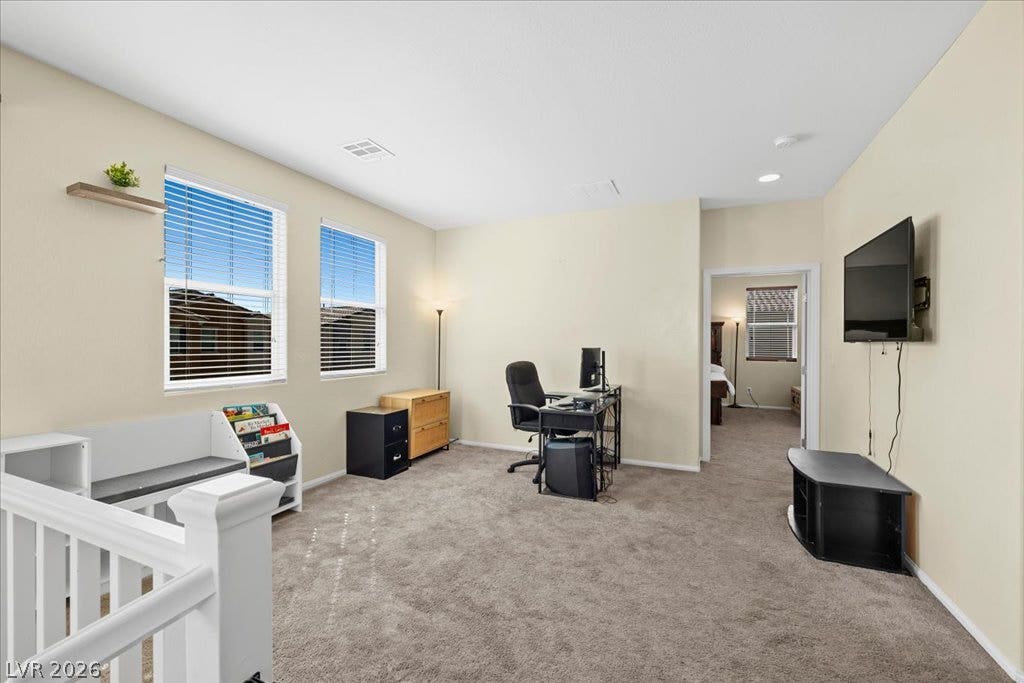 An open upstairs loft area with soft carpet, high ceilings, and abundant natural light.
