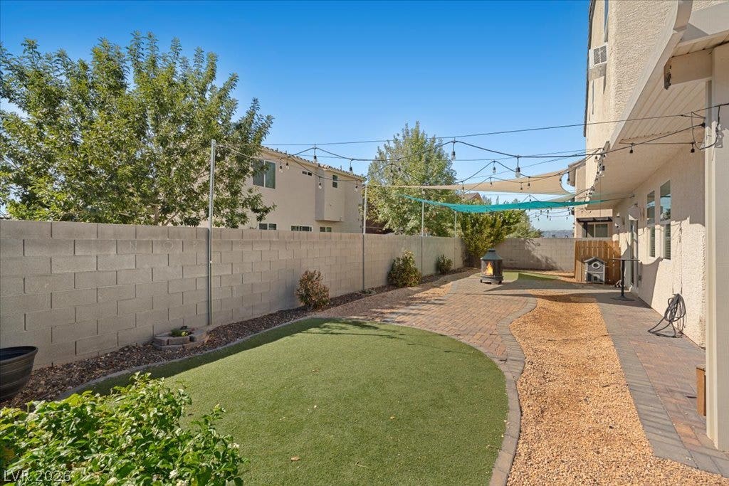 A spacious L-shaped backyard features a paved patio area bordered by a block wall fence.