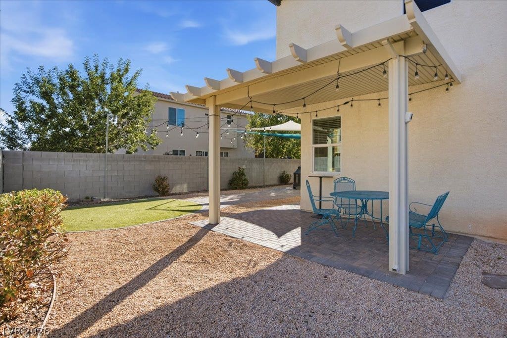 An inviting backyard retreat features a shaded pergola alongside a brick paver patio.