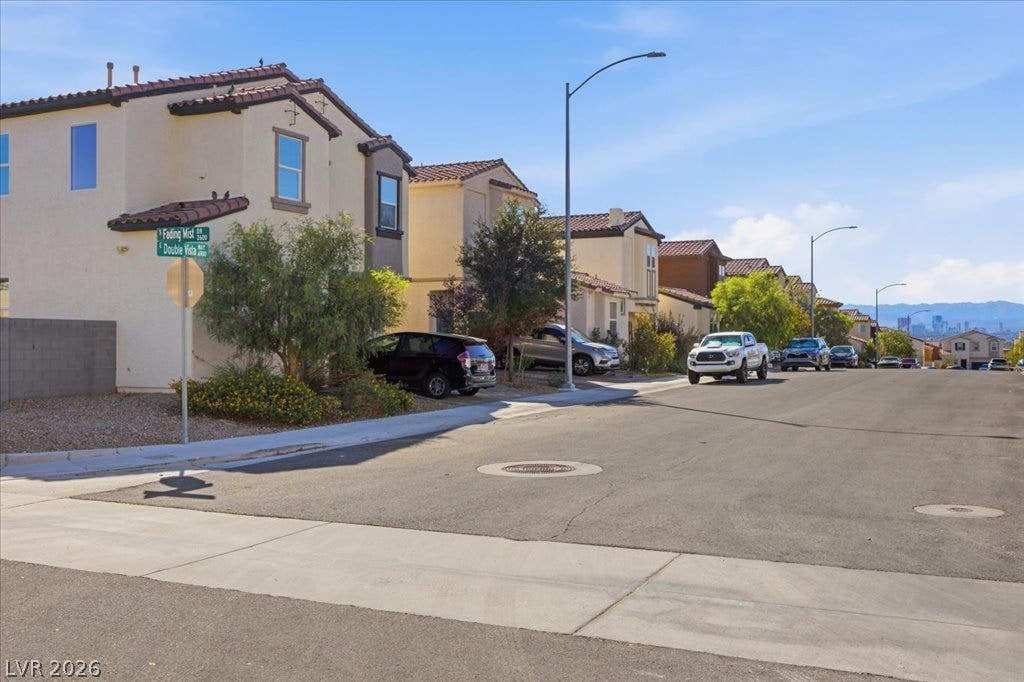Sidewalks and street lights line this quiet suburban residential street under a blue sky.