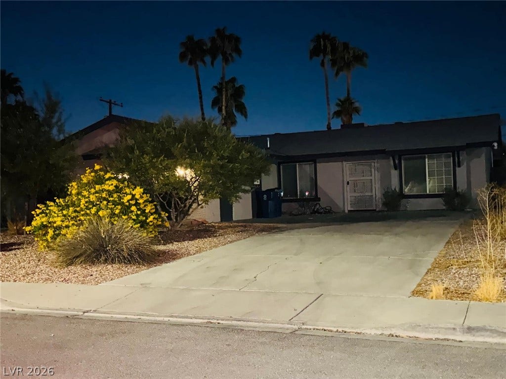 Palm trees rise behind this single-level home featuring a concrete driveway and desert landscaping.