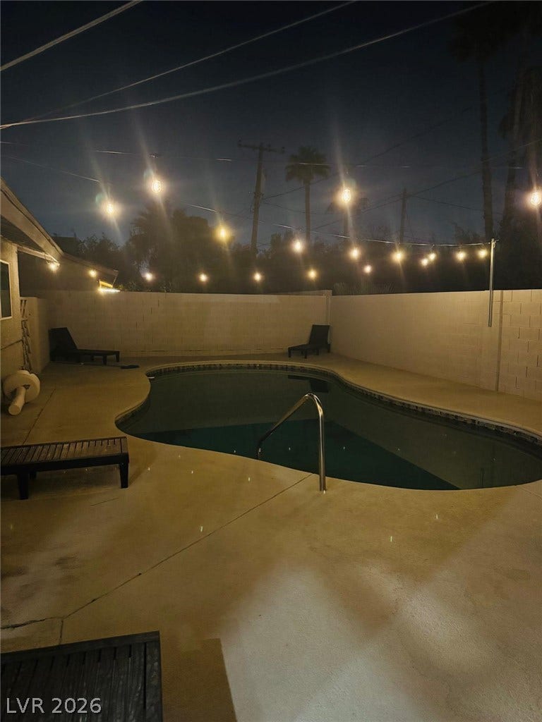 An inviting backyard swimming pool rests beneath a canopy of glowing overhead string lights.