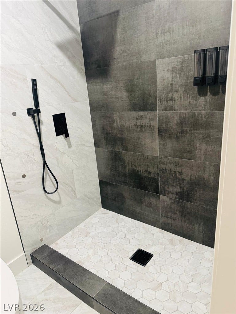 A modern walk-in shower highlights contrast with large-format dark wall tiles and light hexagonal flooring.