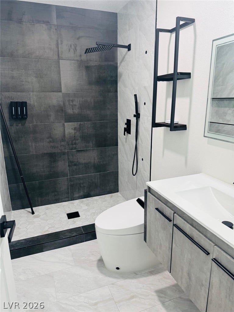 A modern walk-in shower features large-format dark tiling paired with a light stone-tiled floor.