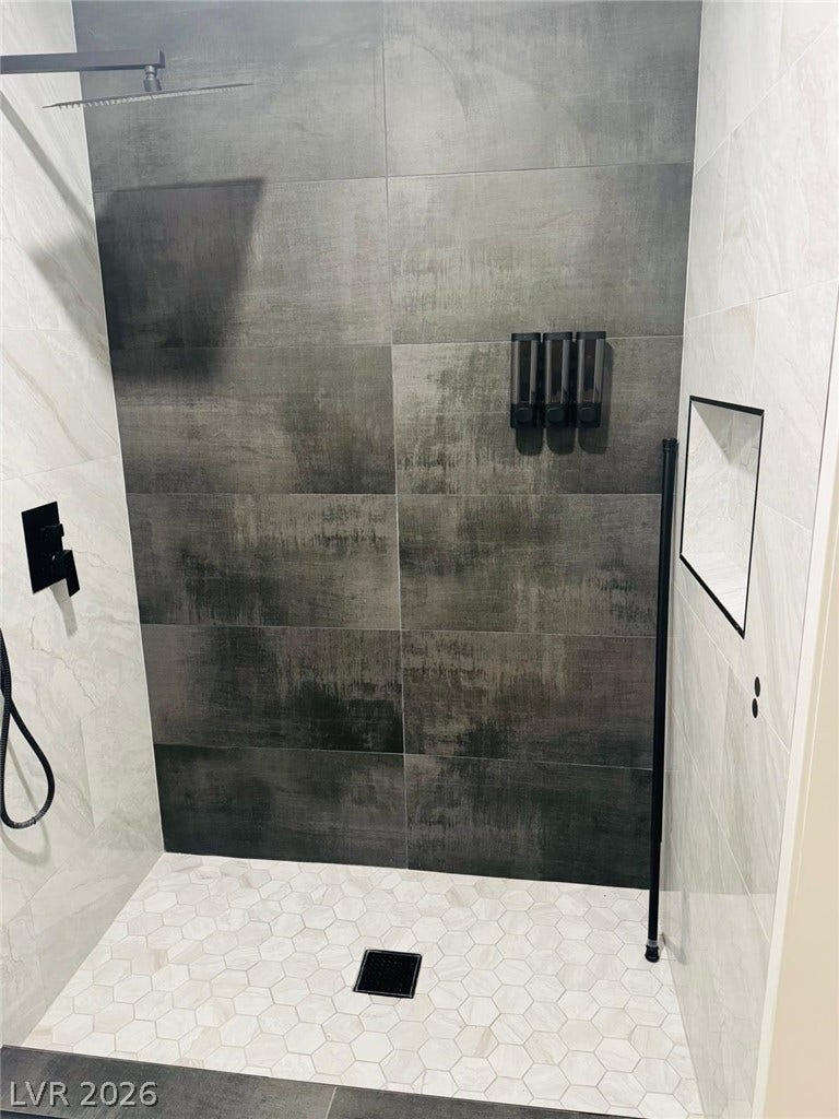 Modern walk-in shower features sleek, large-format wall tiles matched with a geometric mosaic floor.