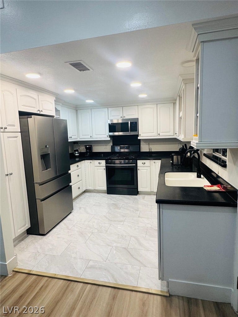 Recessed lighting illuminates classic cabinetry and contrasting dark countertops over light tile flooring.