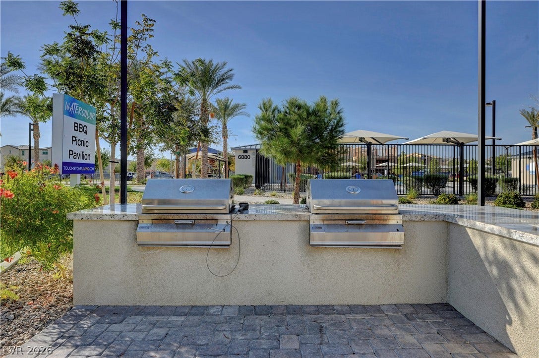 An outdoor grilling station features stone countertops and integrated barbecues set against a paved patio.
