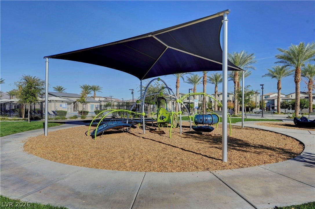 A shaded playground area is surrounded by concrete walking paths and palm trees.