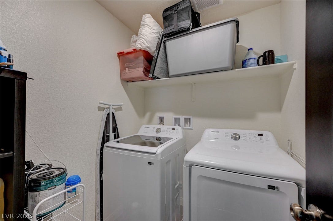 A functional laundry area with overhead storage shelving provides everyday convenience.