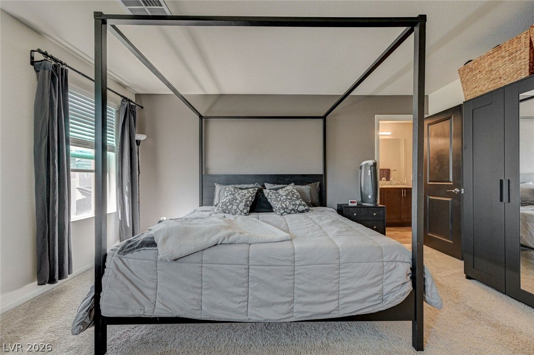 Soft carpeting pairs with tall windows to create a comfortable, well-lit bedroom suite.