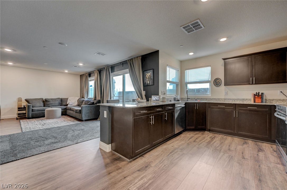 Rich wood-look flooring connects a modern kitchen to an open, light-filled living area.