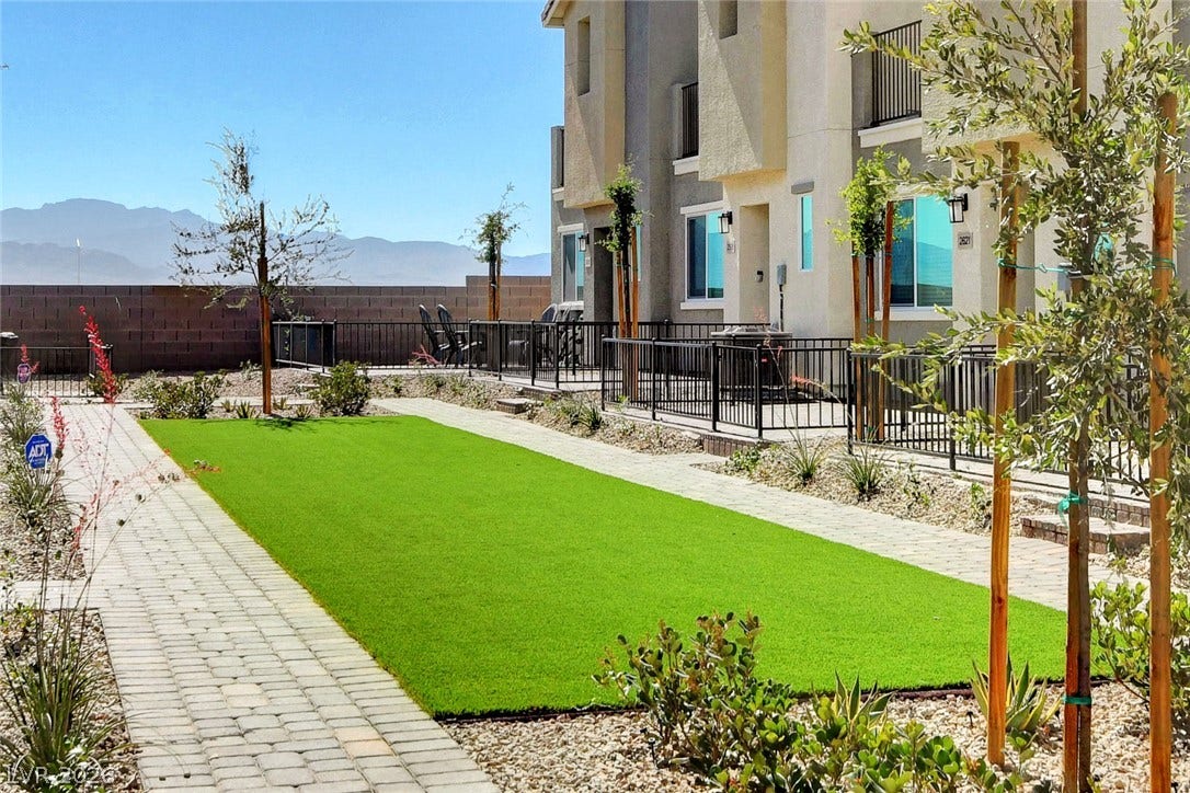Paved walkways flank a green lawn leading to modern townhomes framed by distant mountains.