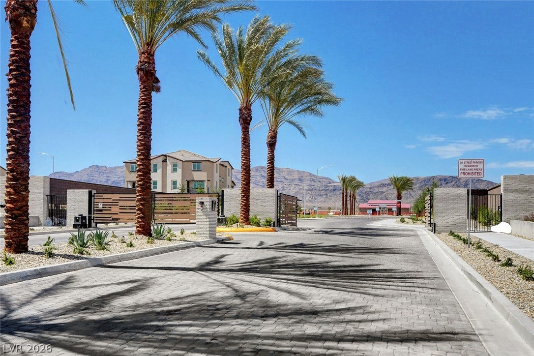 A gated entrance paved with elegant stone features towering palm trees against mountain backdrops.