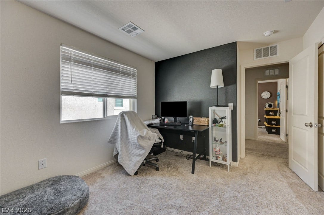 A quiet work space features wall-to-wall carpeting and a wide window.