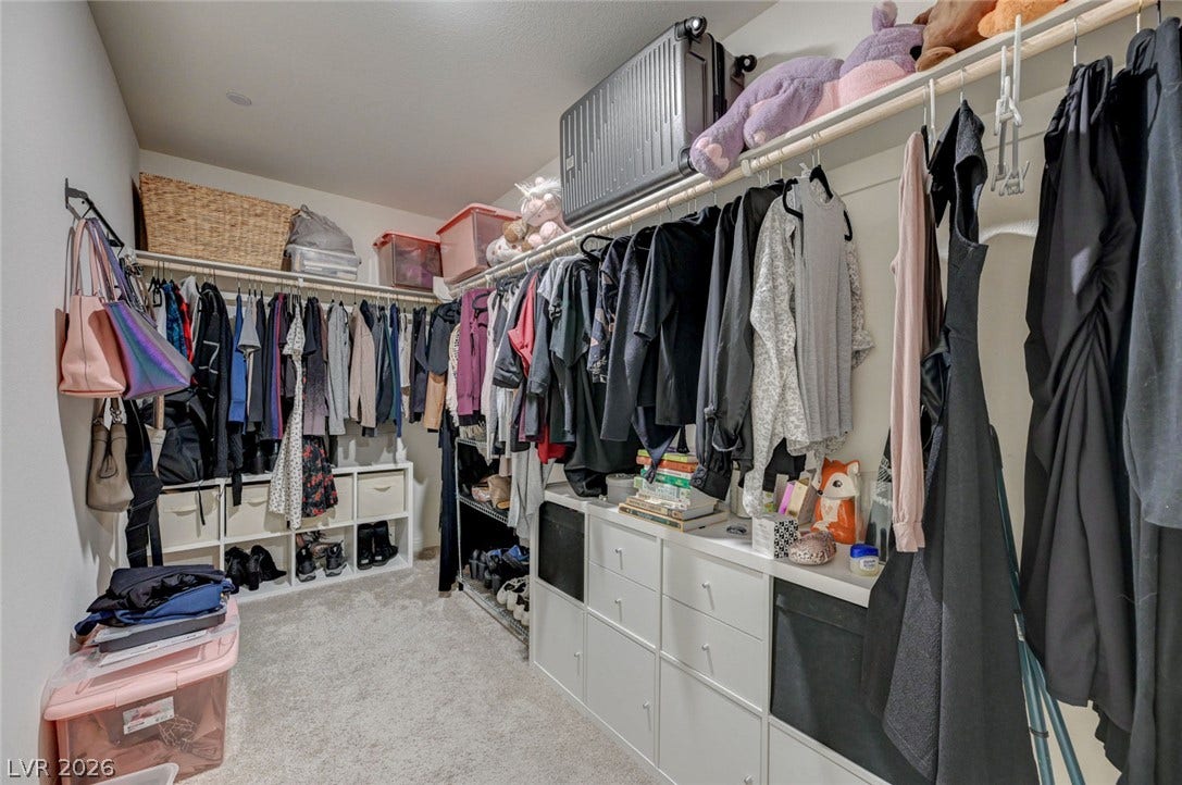 An organized walk-in closet boasts neutral carpeting and built-in shelving.