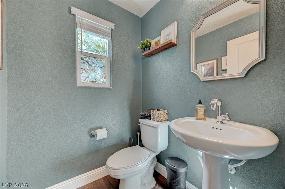 A pedestal sink and classic fixtures complement the warm wood flooring in this powder room.