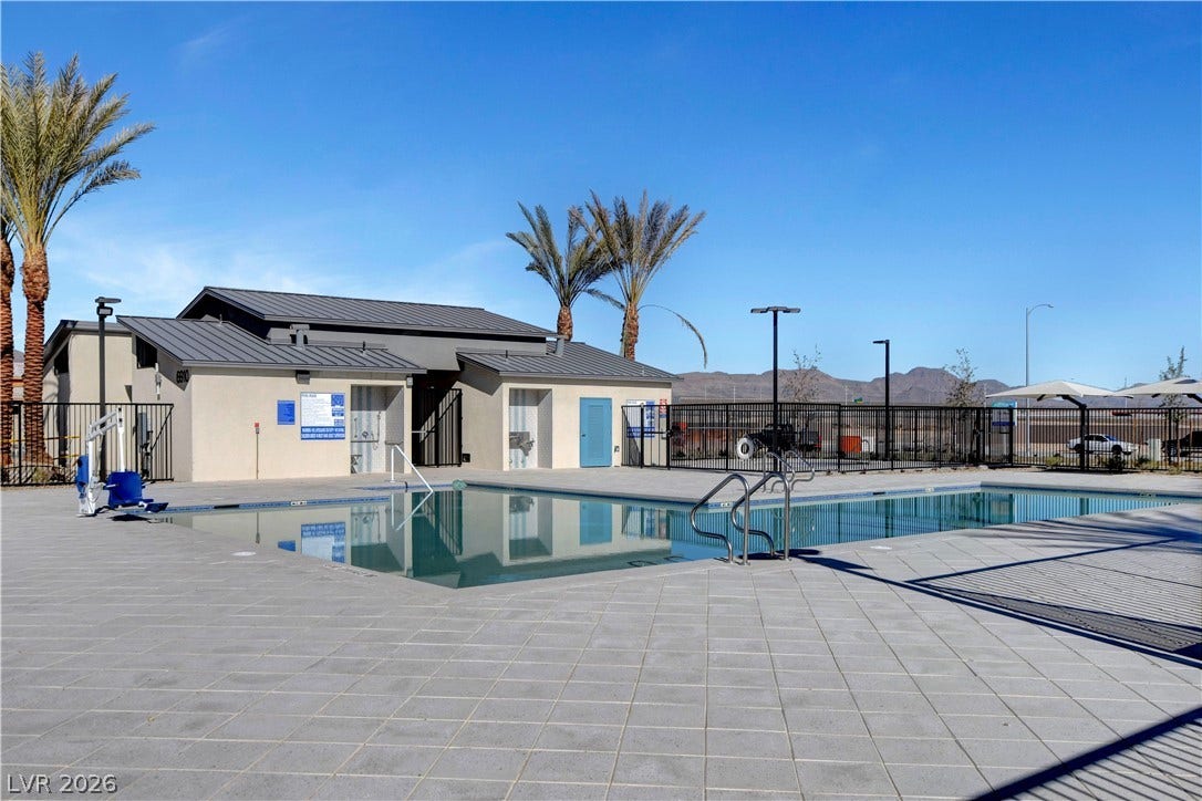 An inviting community swimming pool sits surrounded by paved decking under clear desert skies.