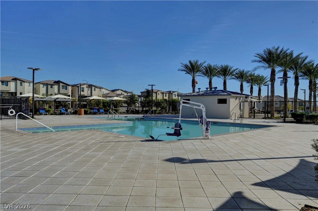A spacious stone patio surrounds this shimmering community pool beneath a clear blue sky.