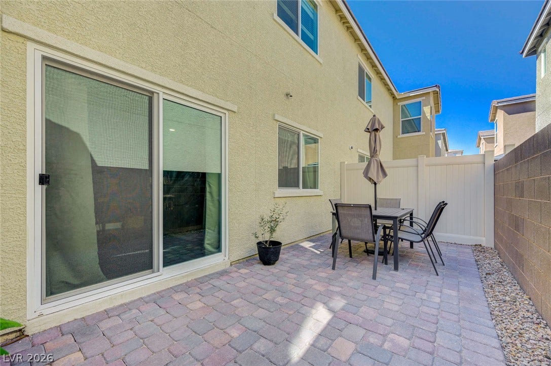 An inviting brick paver patio extends along the stucco exterior beneath clear blue skies.