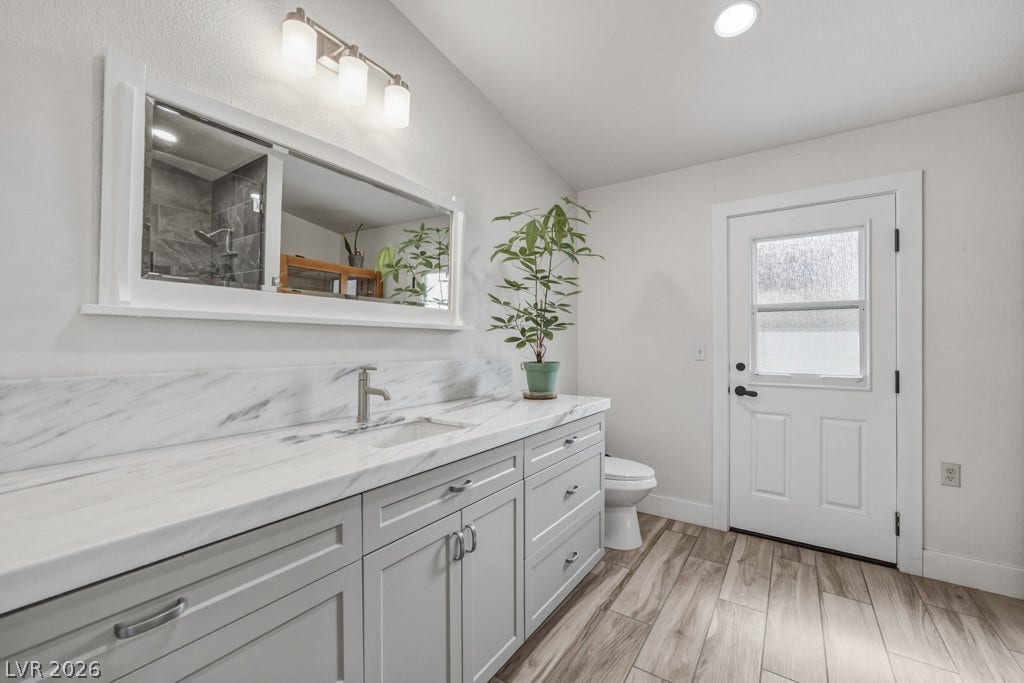 251 W Laval Drive, Henderson, NV 89015 Updated primary bath features an oversized vanity with abundant cabinetry, a sleek marble-look countertop and backsplash, modern fixtures, and access to the backyard.