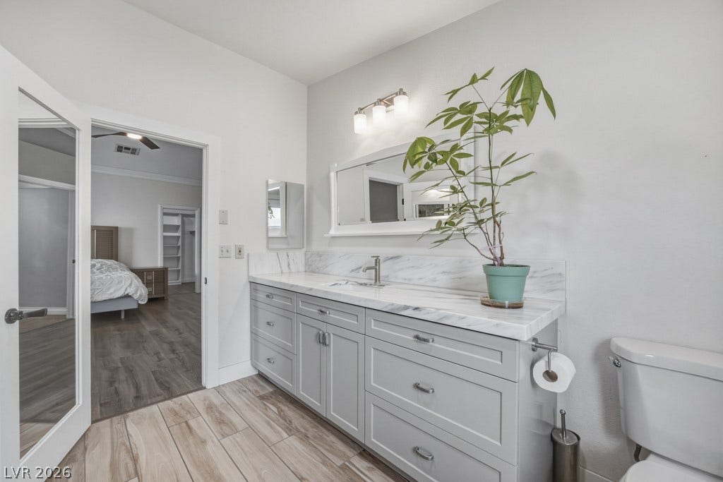 251 W Laval Drive, Henderson, NV 89015 Updated primary bath features a long vanity with abundant cabinetry, a sleek marble-look countertop and backsplash, modern fixtures, and access to the backyard.