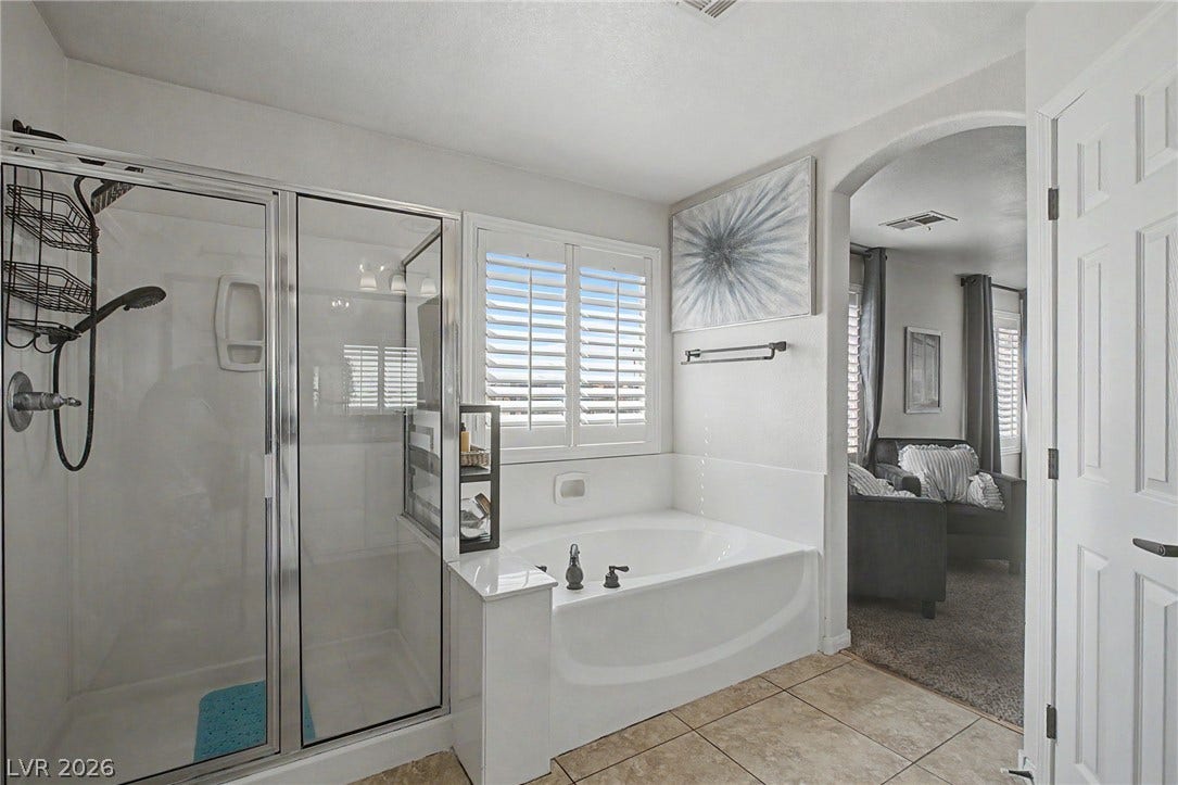 6025 Glenborough Street, North Las Vegas, NV 89115 Tile flooring leads past a glass shower and soaking tub into a neighboring sitting area.