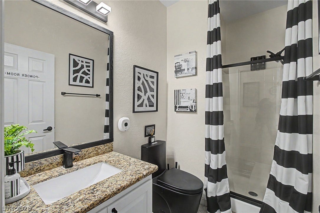 6025 Glenborough Street, North Las Vegas, NV 89115 Modern stone countertops and a glass-enclosed shower highlight this sleek bathroom space.