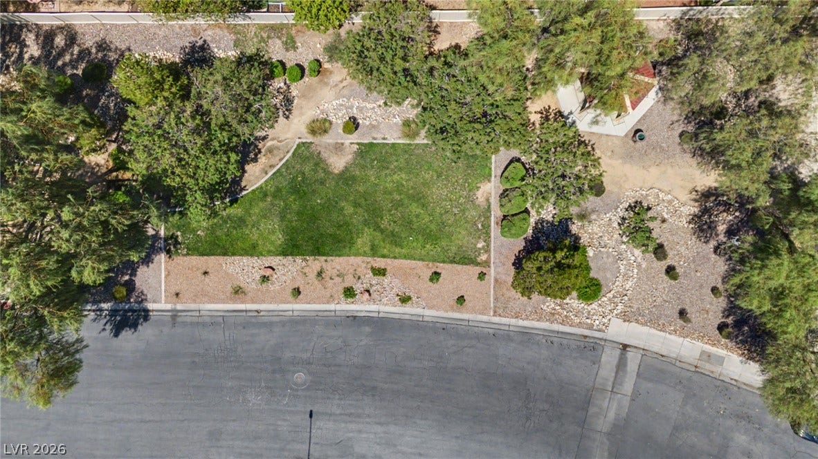 6025 Glenborough Street, North Las Vegas, NV 89115 Mature trees and low-maintenance desert landscaping frame a grassy lawn bordering a curved paved road.