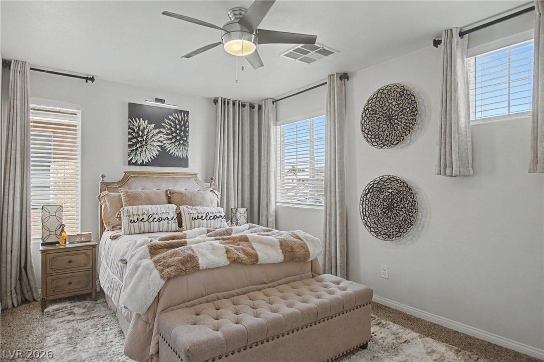 6025 Glenborough Street, North Las Vegas, NV 89115 Multiple windows draw ample natural light across the textured carpet flooring of this bedroom.