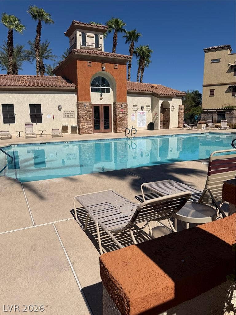 A pristine swimming pool sits alongside a Spanish-style clubhouse surrounded by palm trees.